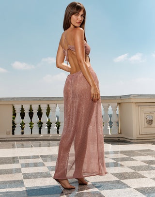 Woman in a long, light pink dress standing on a balcony with a clear blue sky.