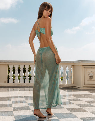Woman in a light green dress standing on a balcony with a clear sky background
