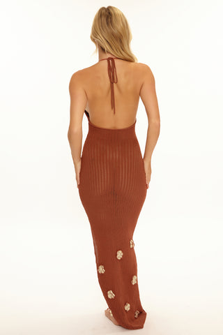 Woman wearing a rust-colored halter neck dress with floral details on a white background