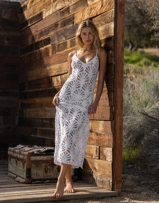 Woman in a white lace dress standing against a wooden wall with a rustic setting.