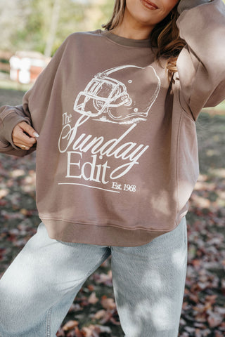 Person wearing a brown sweatshirt with 'The Sunday Edit' logo outdoors.