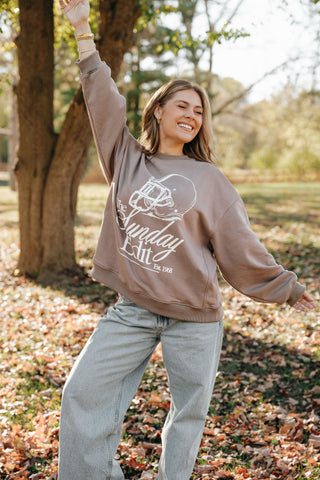 Woman wearing a sweatshirt with a logo in an outdoor setting with trees and fallen leaves.