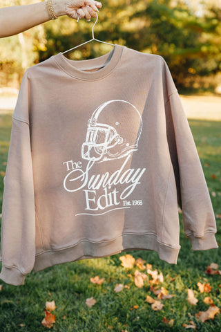 Beige sweatshirt with 'The Sunday Edit' logo on a hanger against a natural background
