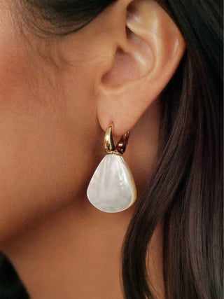 Close-up of an ear wearing a teardrop-shaped pearl earring with gold setting.