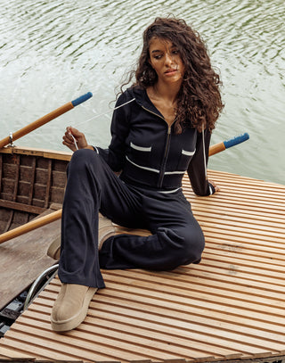 Woman sitting on a wooden dock by a body of water wearing a black tracksuit.