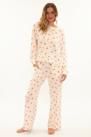 Woman wearing a cream-colored pajama set with red cherry pattern on a white background