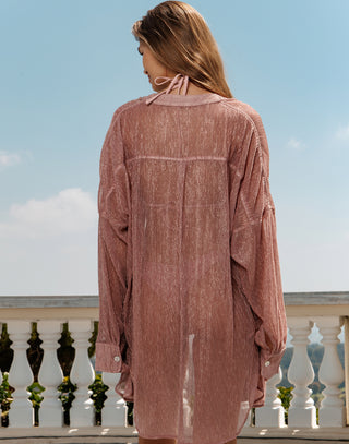 Woman wearing a pinkish-brown dress standing on a balcony with a blue sky background