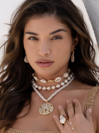 Woman wearing multiple necklaces and a ring with a neutral background