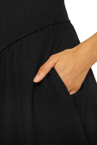 Close-up of a person wearing a black dress with a hand in the pocket against a white background